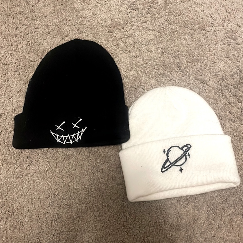 2 beanies one black with a smile x face the other white with a planet